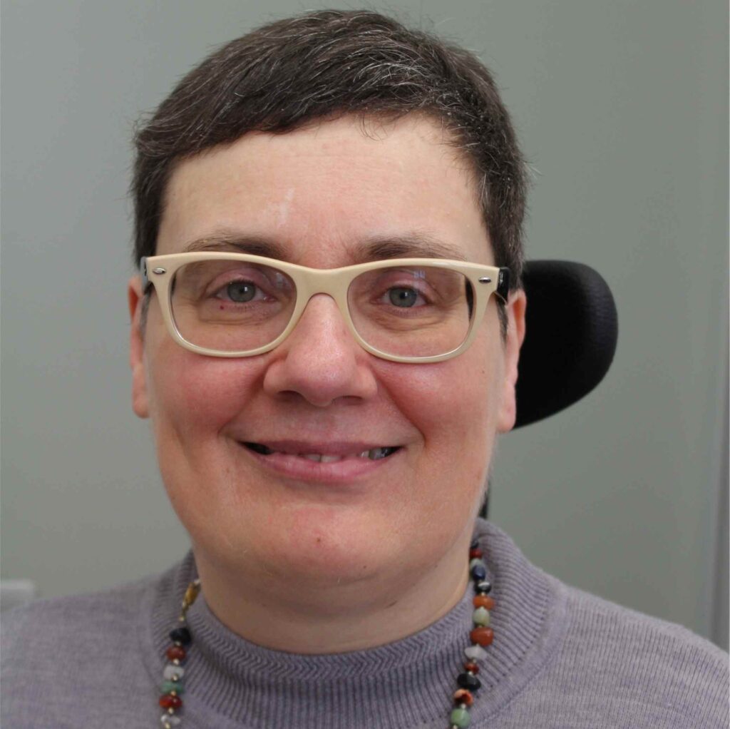 Manuela Lanzinger im Porträt. Kurze Haare, gelbe Brille, grauer Pulli.