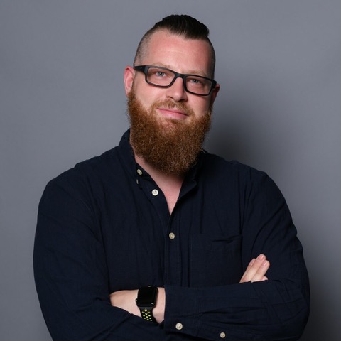 Wolfgang trägt ein schwarzes Hemd, hat einen rötlichen Vollbart und trägt eine schwarze Brille.