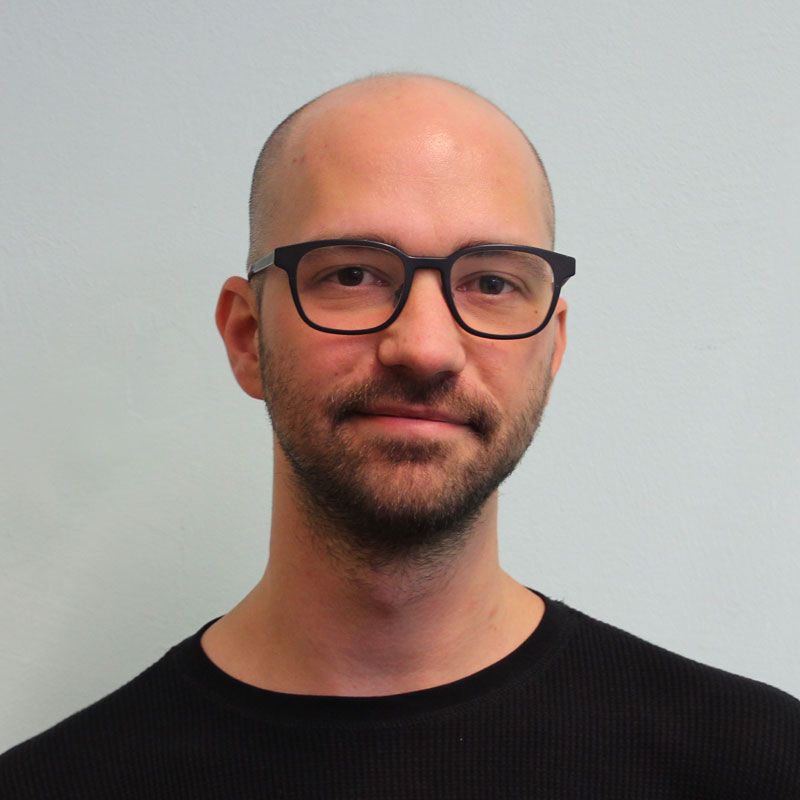 Oliver Wurm ist ein junger Mann mit Glatze, einer Brille und einem Bart.